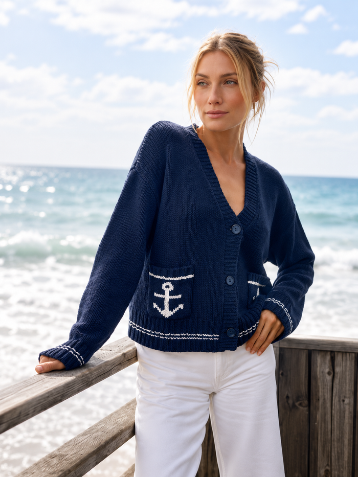 Woman wearing a navy cardigan with an anchor design by the ocean.
