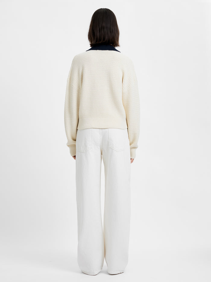 Person wearing a cream sweater and white pants on a light gray background