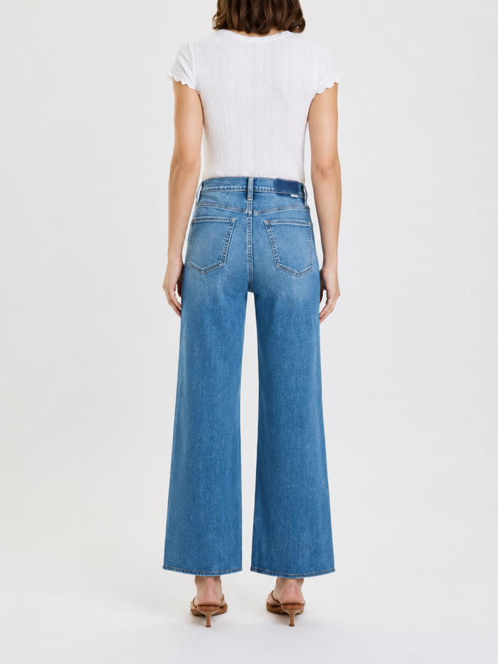 Person wearing blue jeans and a white top on a plain background
