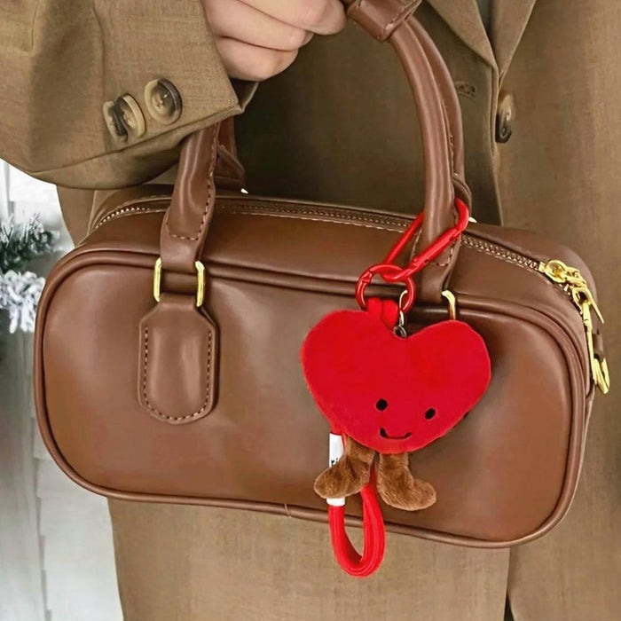 Model holding a brown handbag with smiling heart bag charm.