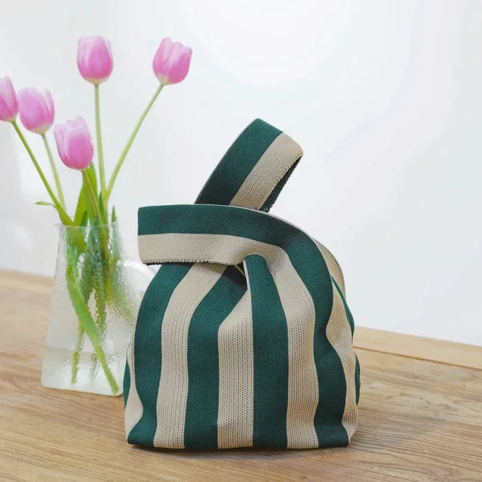 A forest green and light khaki stripe woven handbag next to pink tulips, highlighting a soft spring aesthetic.