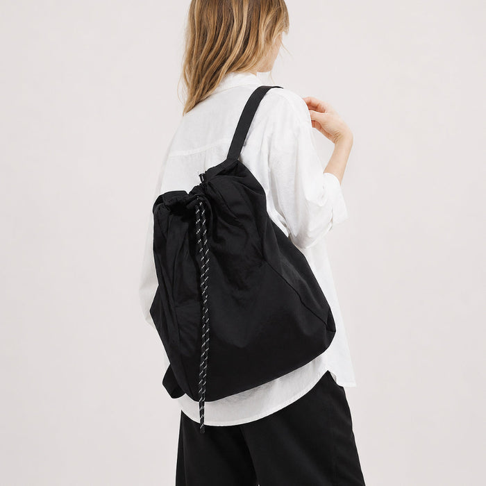 Model wearing the classic black 2-way drawstring backpack over one shoulder as a tote.