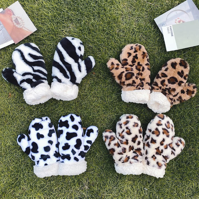 Flat lay animal print fluffy mittens on grass (zebra, cow, leopard) with white sherpa cuffs; cozy winter warmth.