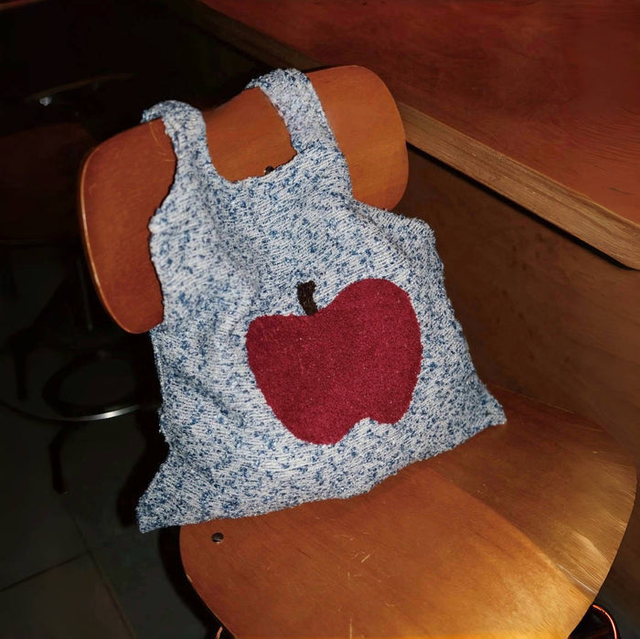 Close-up of Blue and white knit polyester bag with a large red apple design and two grab straps .