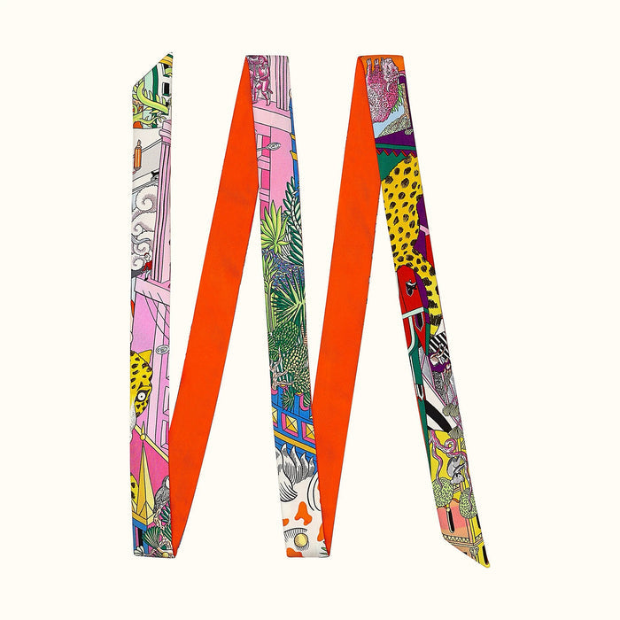 Angled view of Orange polyester skinny scarf with vibrant artistic print, featuring diverse patterns and colors.