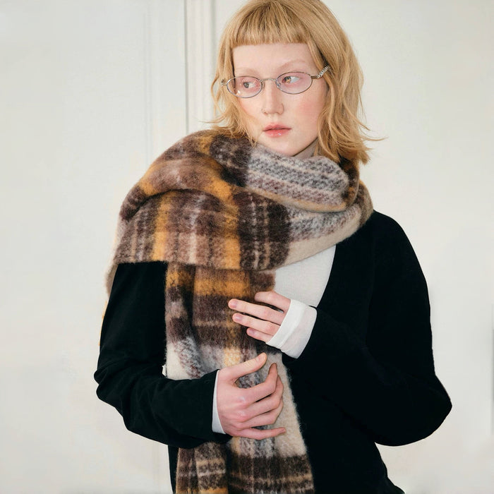 Model wearing cozy Autumn Ember Plaid Scarf, a wool blend in warm brown, gold, and cream tones in yellow.