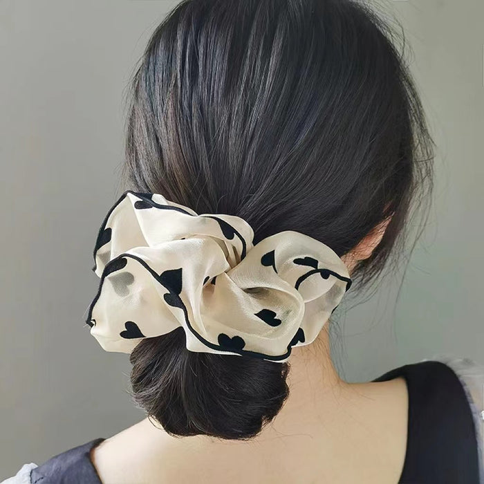 Model wearing satin scrunchie with white background, black heart pattern and black trim.