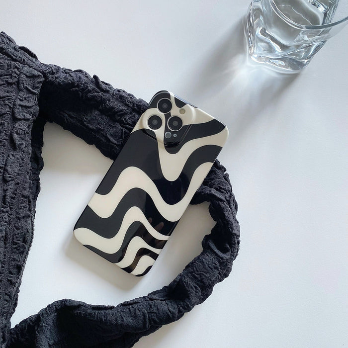 Abstract wavy acrylic phone case on white surface with strap. Aesthetic lifestyle flatlay for desk setup inspiration.