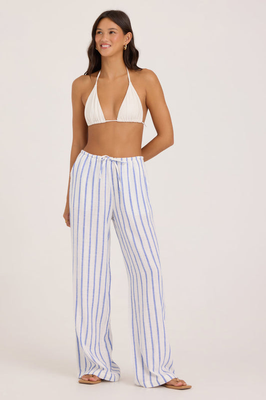 Woman wearing a white bikini top and blue striped pants on a white background