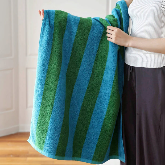 Model holding up a fully unfolded Bold Color Striped Bath Towel in blue-green, easy for gym, travel, and weekends.