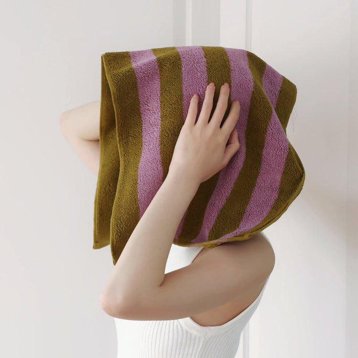 Model holding a Bold Color Striped Face Towel in Rose Violet -Yellowish Brown to dry her hair.