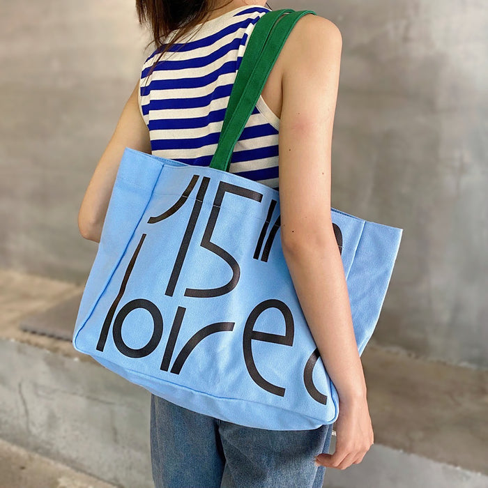 Model wearing a blue Bold Letter Canvas Tote Bag, trendy bold graphic bag for Urban Creatives and daily utility.