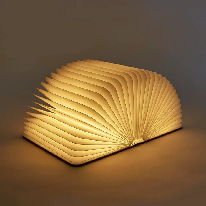 Walnut wood and paper book lamp, open to a glowing fan shape, emitting warm LED light.