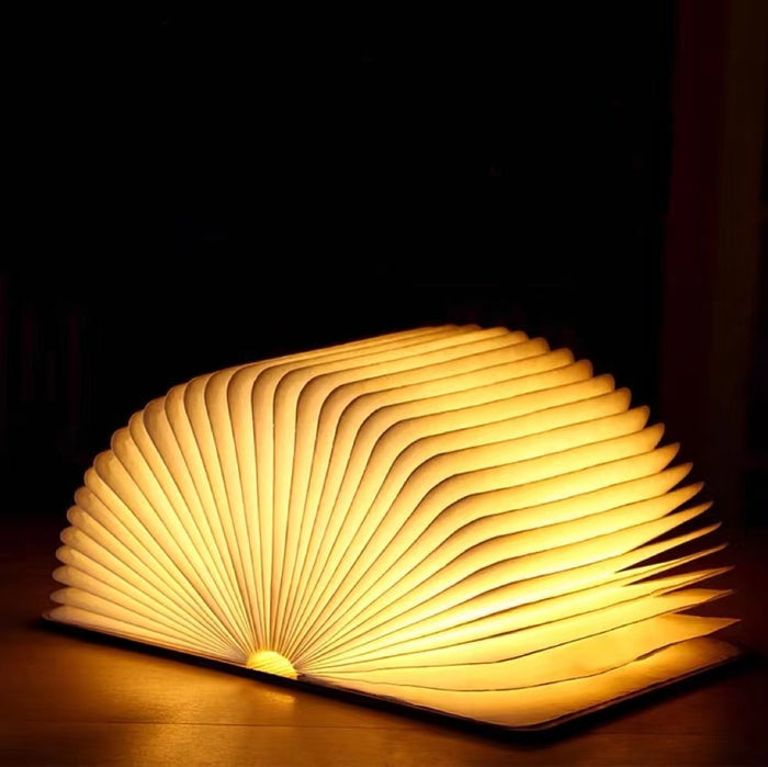 Walnut wood book lamp opened to a fan shape, emitting a warm LED glow on a dark surface.
