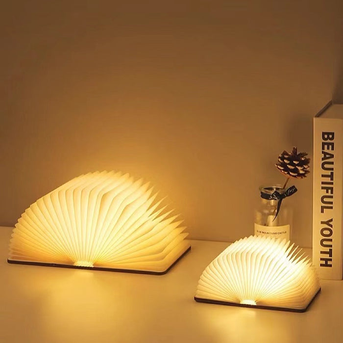 Two open book lamps with glowing paper pages and walnut wood covers, illuminating a desk.