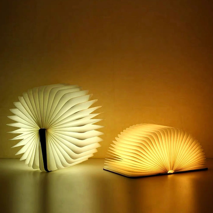 Two glowing book lamps made of wood and paper, one open fully, the other partially, emitting warm LED light.