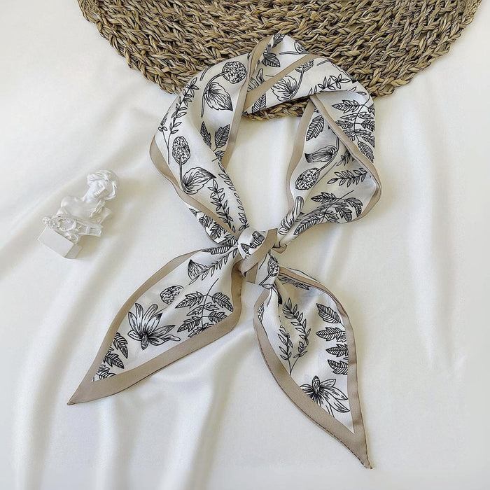 Front view of White polyester silk scarf with black botanical pattern and tan border, tied in a knot in khaki.