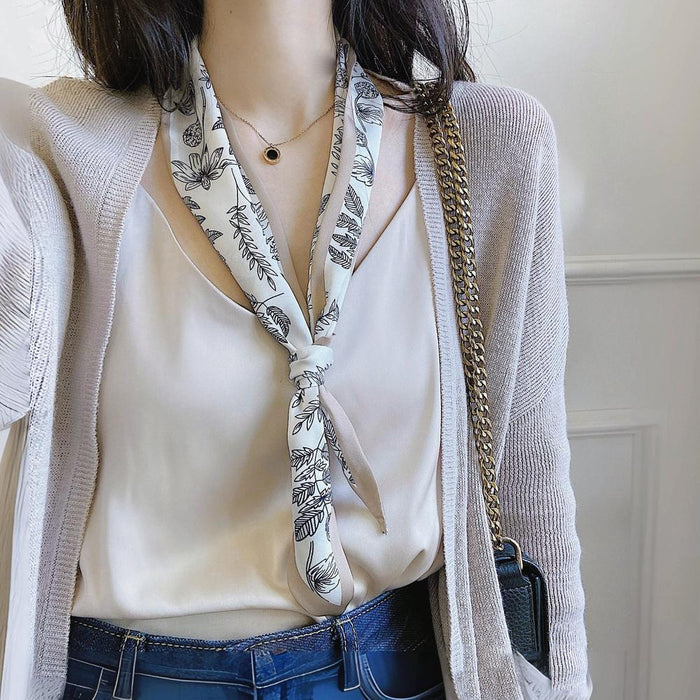 Model wearing a White polyester silk scarf with black botanical pattern, tied at the neck in beige, great for office.
