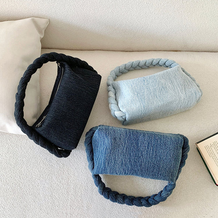 Close-up of Three braided handle denim handbags in dark blue, light blue, and black on a white couch.