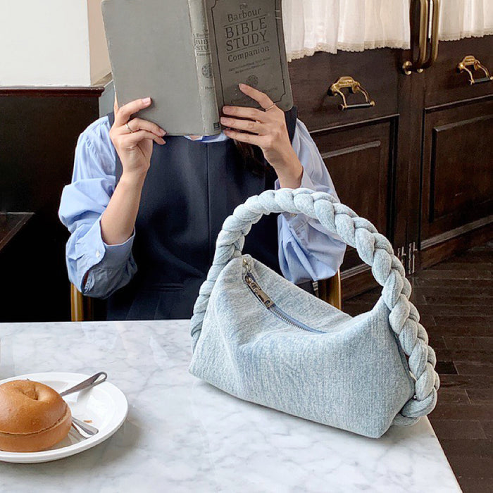 Front view of light blue Braided Handle Denim Handbag putting on a table, easy for commuting and weekends.