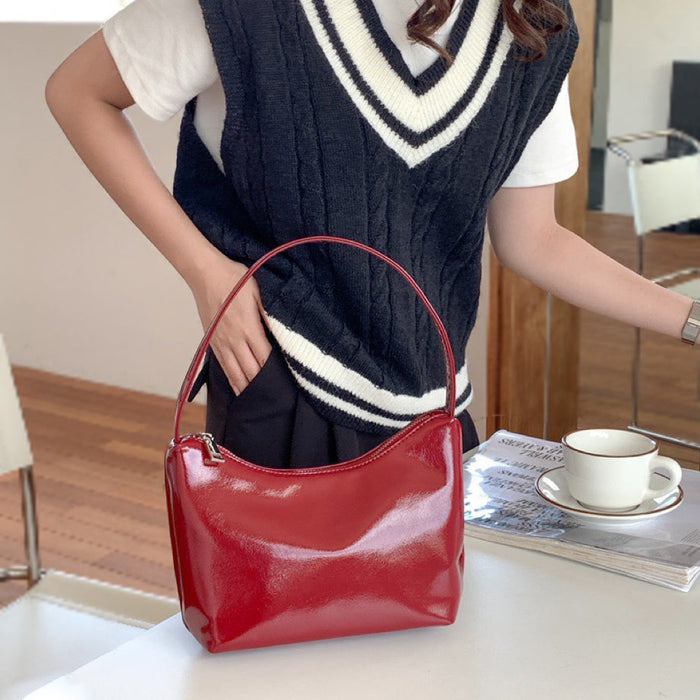 Bright red patent leather shoulder bag on a table; high-gloss mirror finish and minimalist 90s silhouette.
