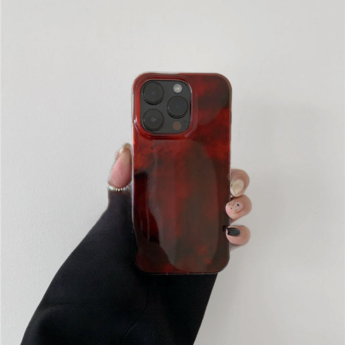 Hand holding a glossy burgundy acrylic phone case. Real-life grip showcasing the unique flux pattern and shine.