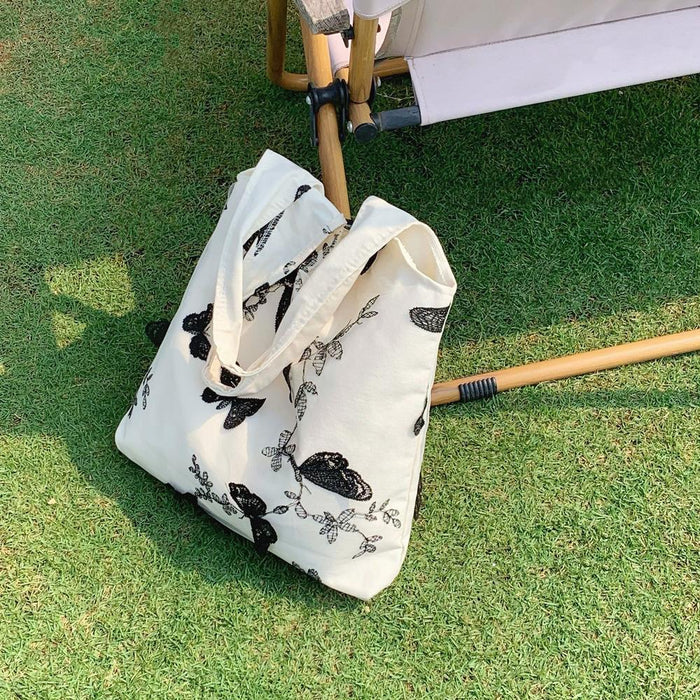 White canvas tote bag with black butterfly embroidery on green grass.
