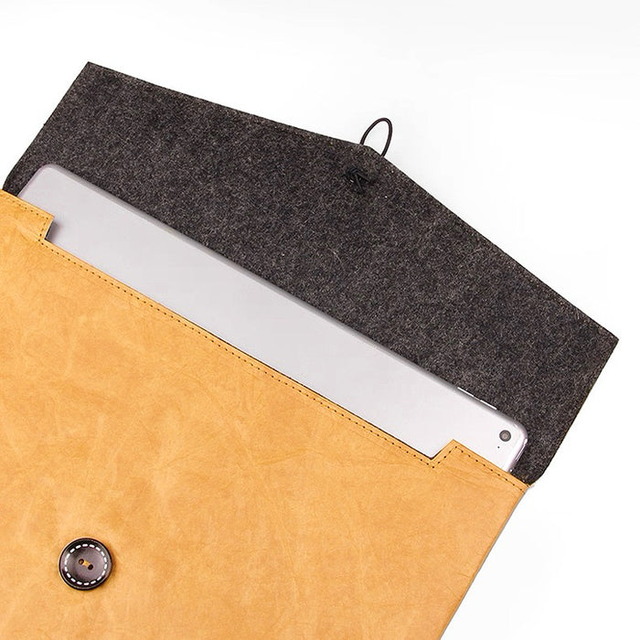 Tan Tyvek laptop sleeve with a dark felt interior, button and cord closure, holding a silver laptop.