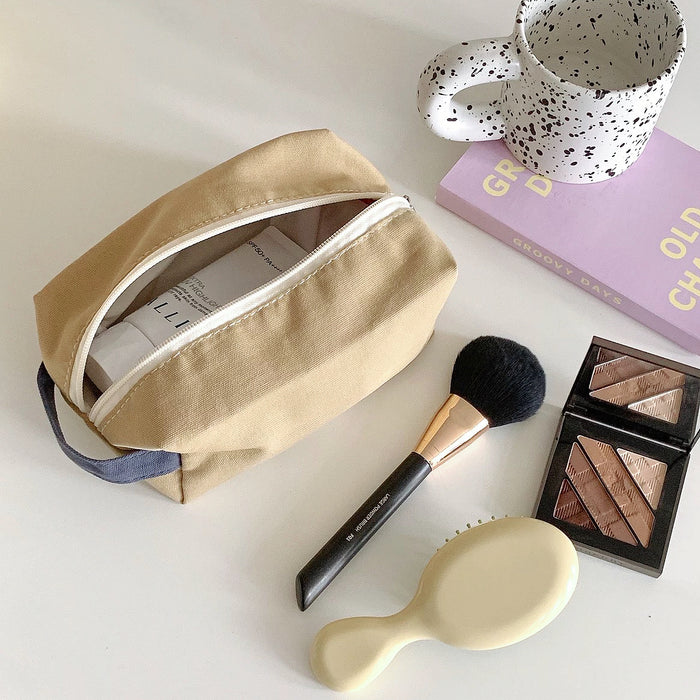 Top view of khaki canvas makeup bag on a table with a brush and shadow; minimalist aesthetic cosmetic pouch.