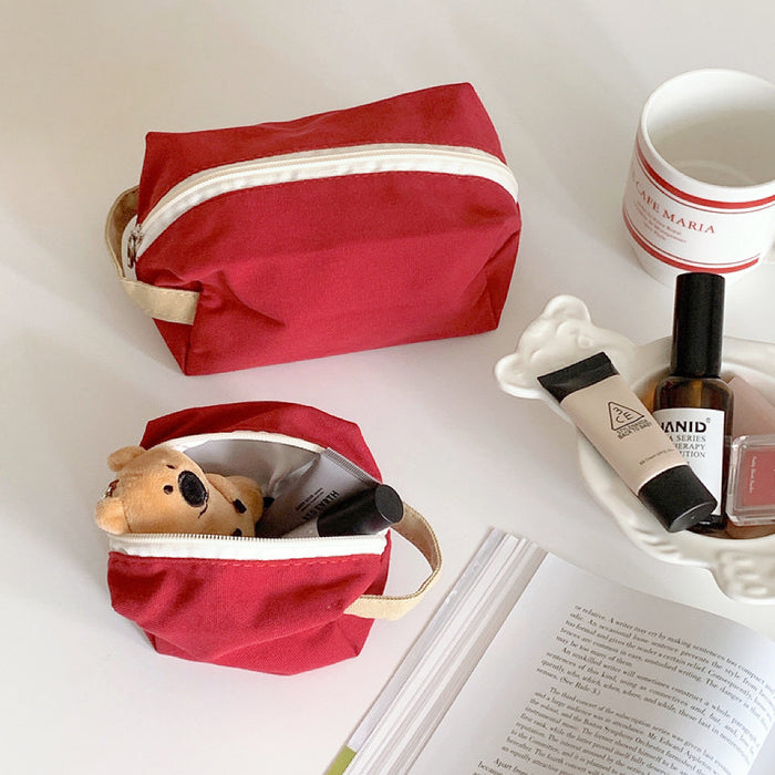 Open red canvas pouch with a small teddy bear and cosmetics; portable travel organizer for personalized items.