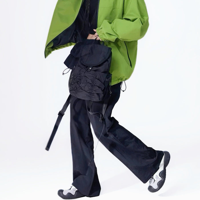 Model holding a black pleated backpack, trendy urban utility look for fashion-forward commuters.