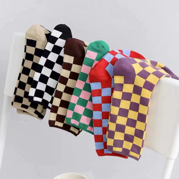 Six pairs of checkered socks in different colors hanging on a chair.