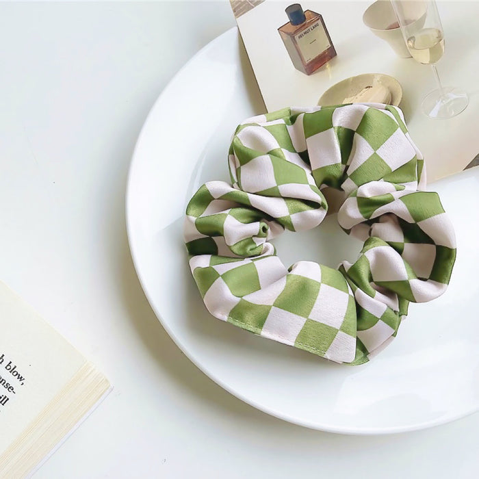 Flat lay of checkerboard satin scrunchie in green, great for everyday styling and gifting.