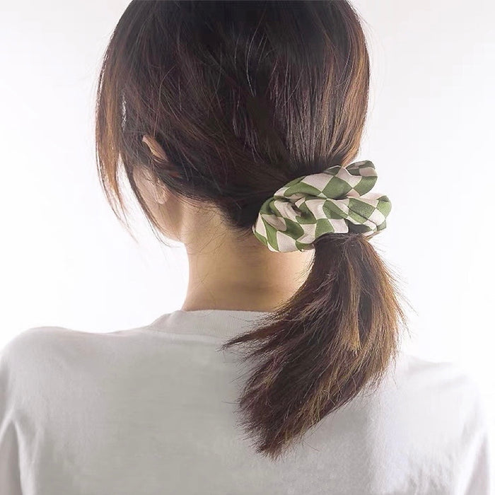 Model wearing checkerboard satin scrunchie in green, ideal for quick updos and ponytails.