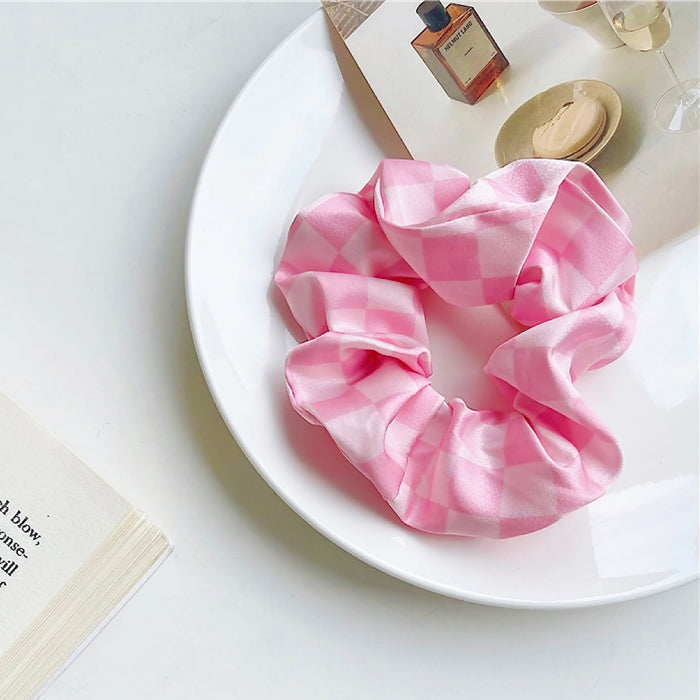 Angled view of checkerboard satin scrunchie in pink, great for everyday styling and gifting.