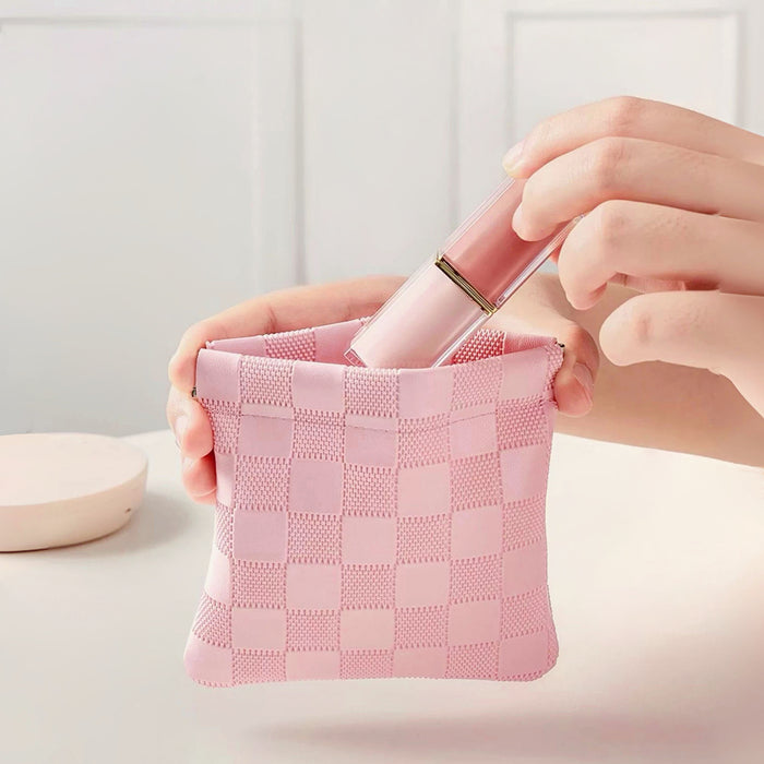 Hands placing lipstick into pink checkered self-closing pouch; flexible woven bag for makeup touch-ups.