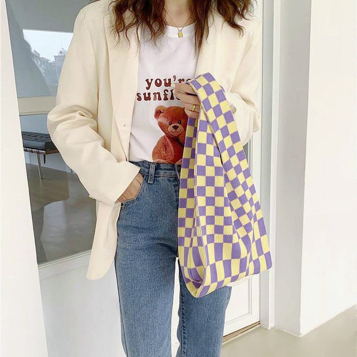 Model styling a purple and yellow checkered woven tote bag handheld.