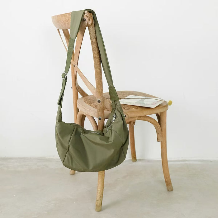 The army green ruched crescent bag displayed on a wooden chair.