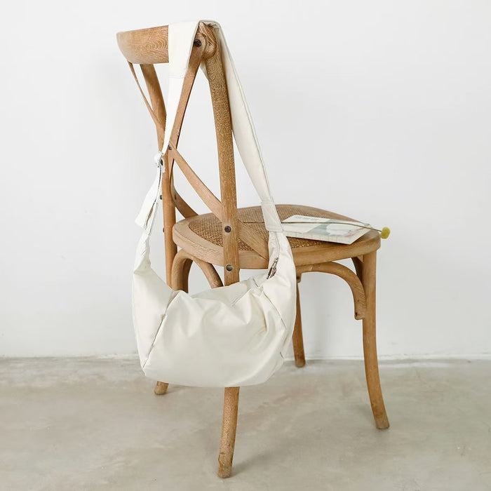 The off-white ruched crescent bag displayed on a wooden chair.