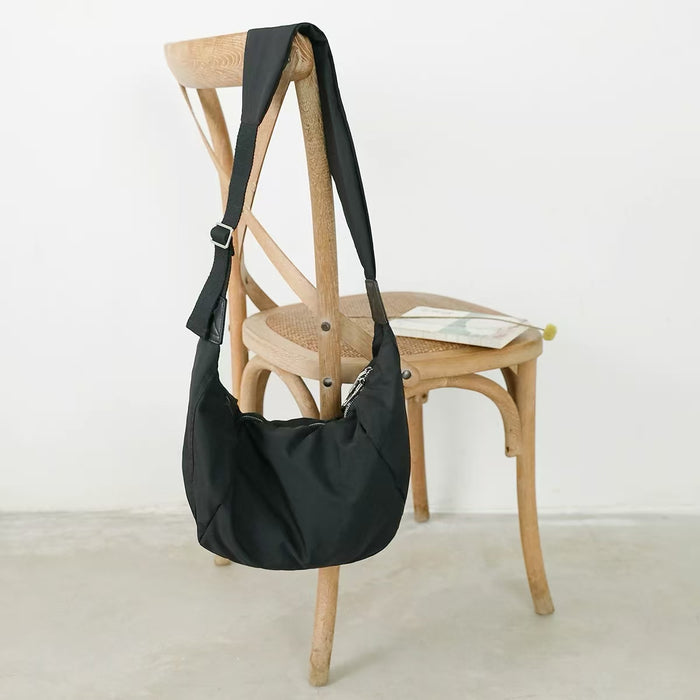 The classic black ruched crescent bag displayed on a wooden chair.