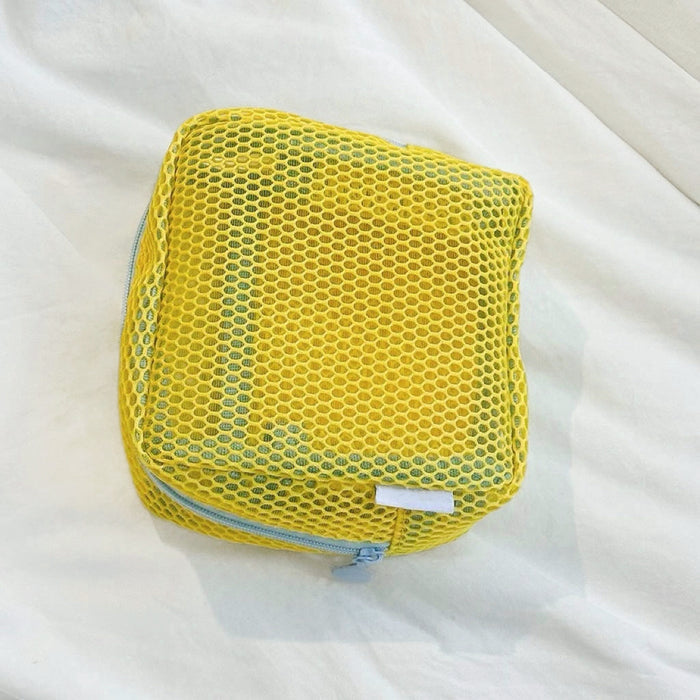 Yellow Chroma mesh pouch with blue zipper on fabric; square zip organizer for cosmetics and travel items.