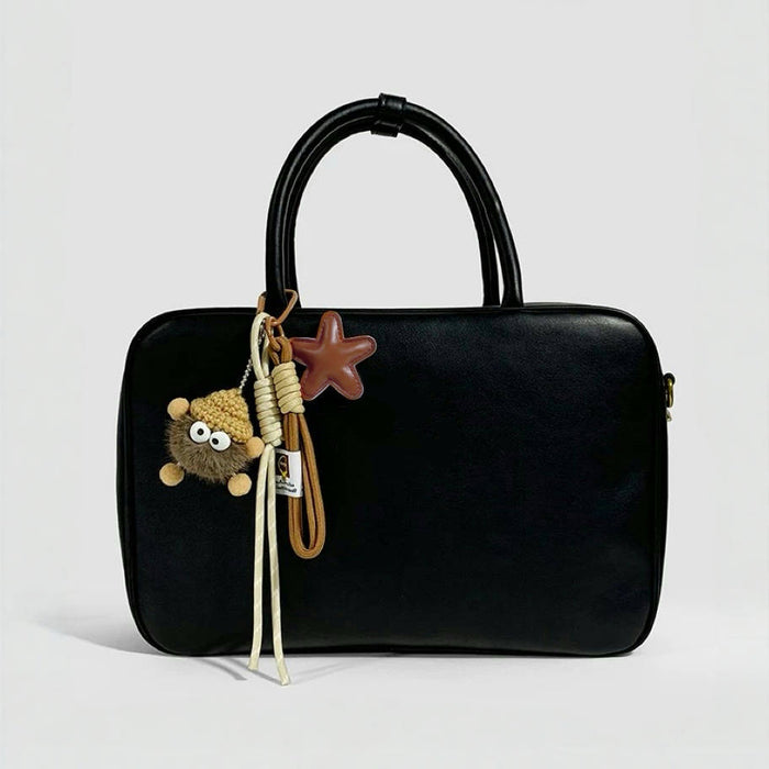 Brown coalball star charm attached to a minimalist black leather tote bag; stylish bag personalization for daily commute.