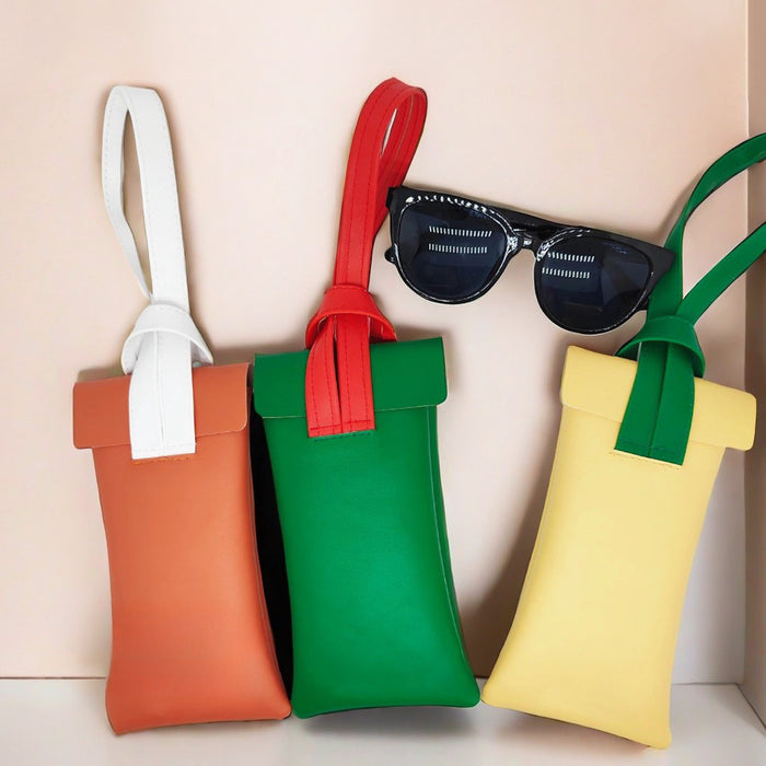 Three color block PU leather glasses cases in rust brown, green, and cream yellow with contrasting straps.