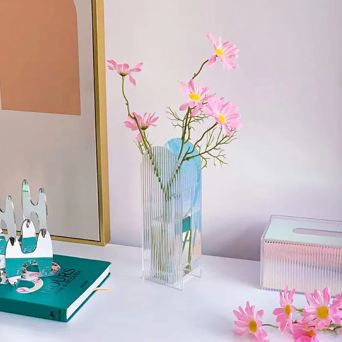 Front view of Colorful acrylic ripple vase, holding pink flowers, on a white desk.