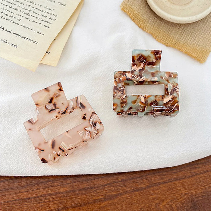 Two small square acrylic hair claws shown together, one in light pink tortoise shell and one in blue-green.