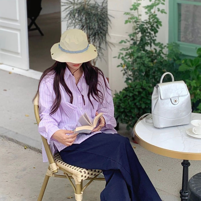 Woman  wearing a beige nylon Colorband Flip Bucket Hat with a blue band, reading outdoors.