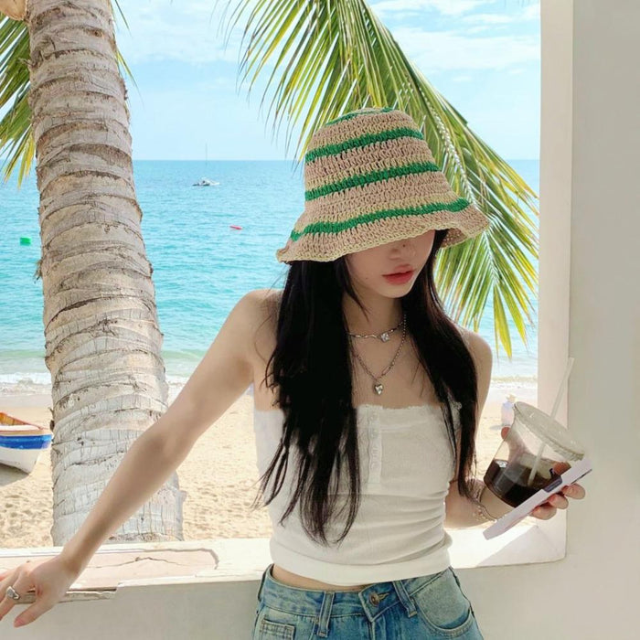 Person at the beach wearing a green striped straw hat, ideal for breathable and stylish vacation wear.
