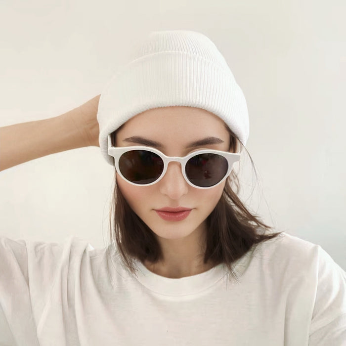 Woman wearing white knitted beanie with sunglasses, a chic accessory for urban winter street style.