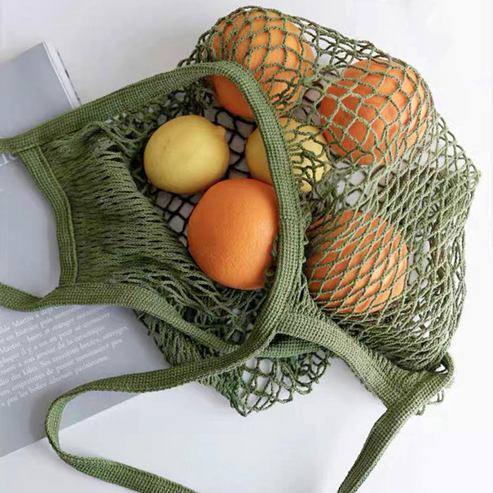 Close-up of Green cotton net shopper bag filled with oranges and lemons, ideal for errands and gifting.