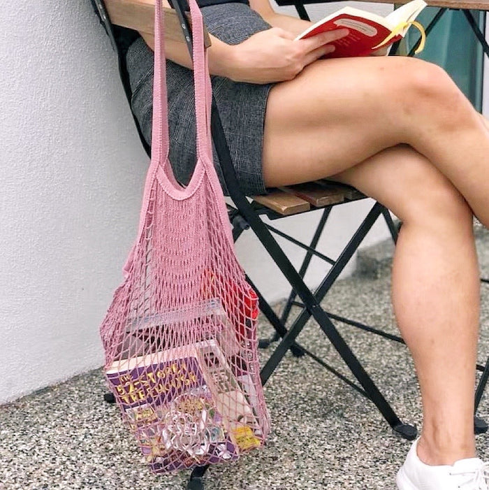 Model carrying a pink net shopper bag handheld, great for daily carry and travel.